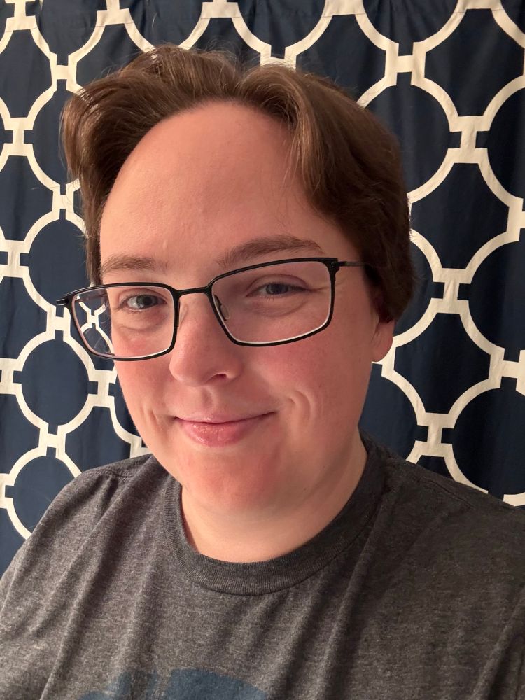 A selfie facing the camera in front of a blue and white curtain, featuring my new short hair. 