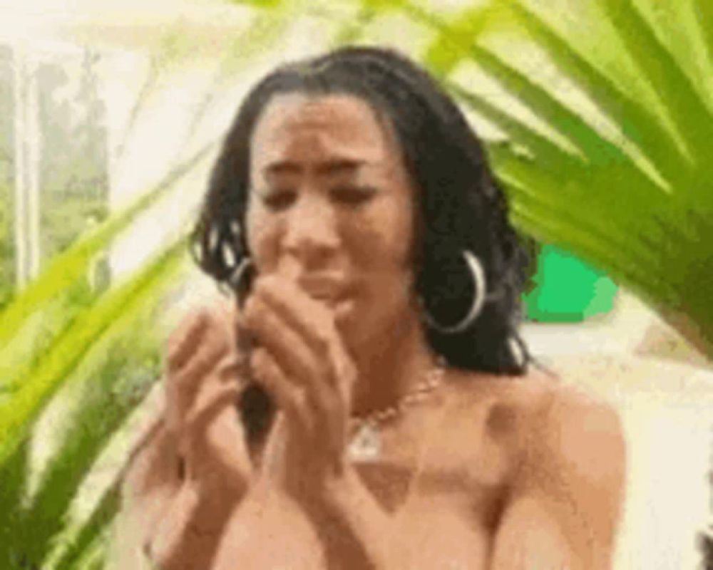 a naked woman is crying while holding a cell phone in her hands in front of a palm tree .