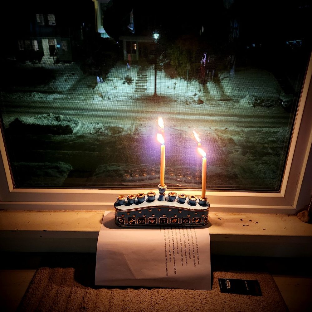 A menorah sits on a windowsill with two candles lit, the shamash and the first night's candle.