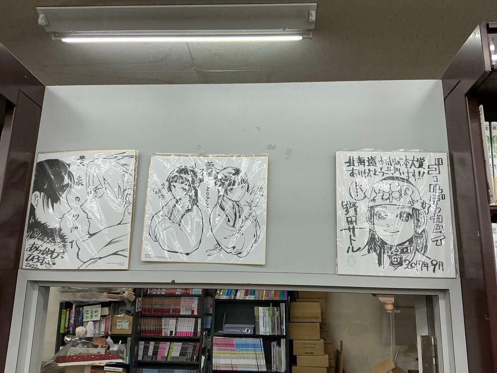 Three manga artists’ sketches. One on the left by Hiromu Awakawa of characters I don’t recognise. The middle one is of Maomao from The Apothecary Diaries, the right one of Asirpa from Golden Kamuy.