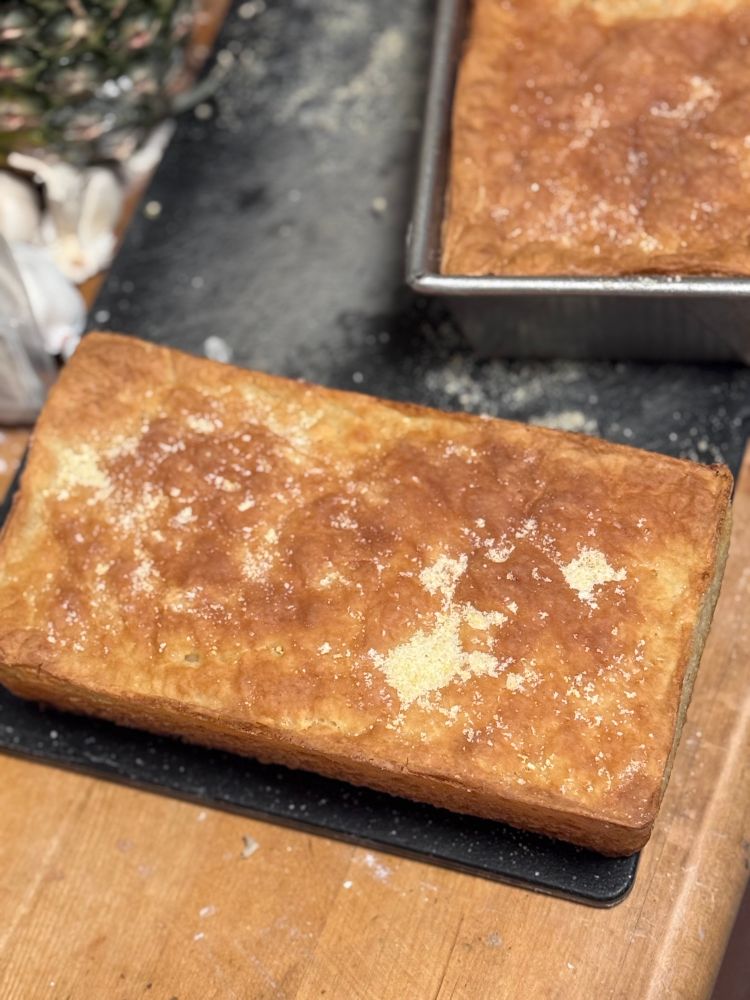 A picture of a loaf of English muffin bread with a loaf sitting next to it still in the loaf pan. Both are sitting on a black cutting board 
