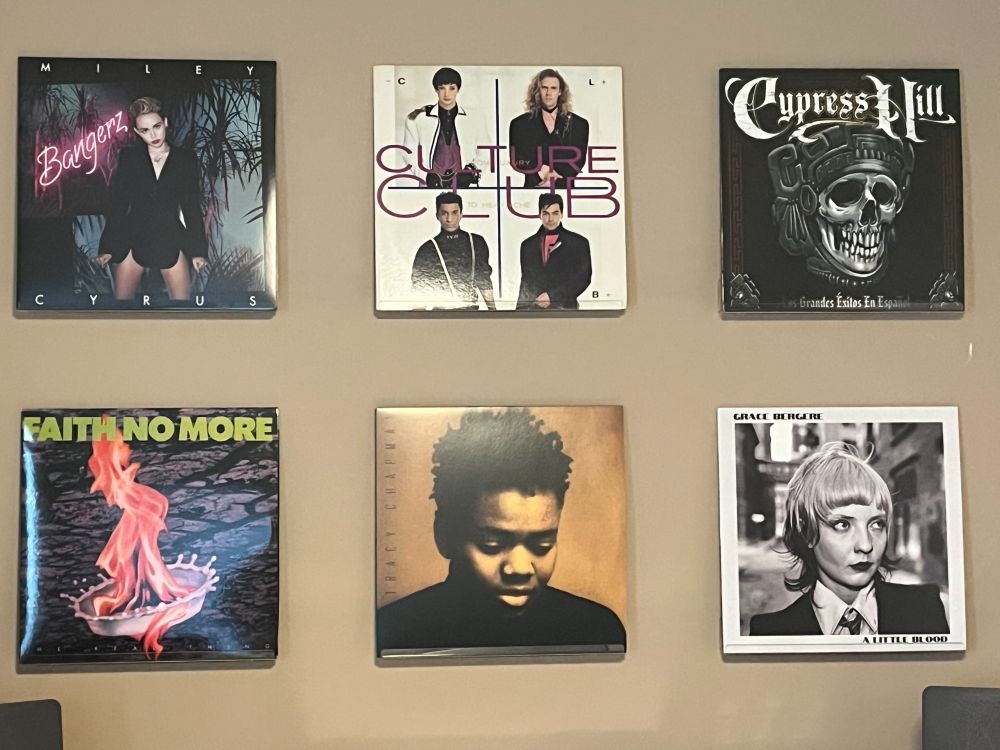 Six albums displayed on a beige wall by artists Miley Cyrus, Culture Club, Cypress Hill, Faith No More, Tracy Chapman, and Grace Bergere