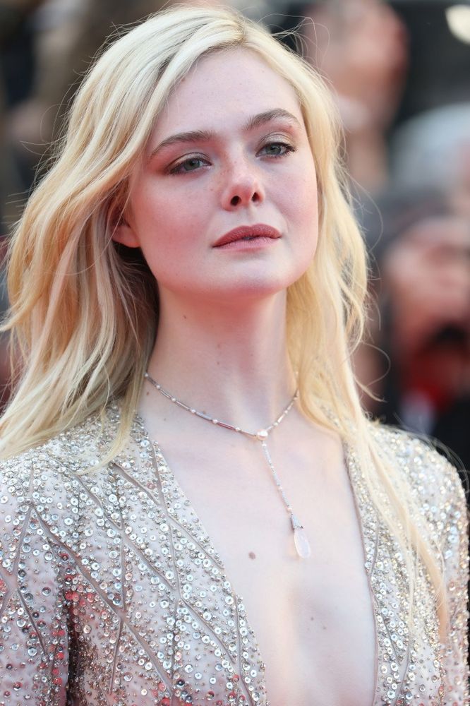 The actress, Elle Fanning, posing for a photograph wearing a fancy silver/white dress.