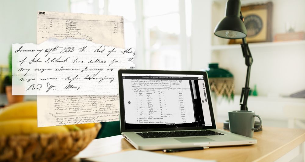 A laptop sits on a modern desk, a desk light to the right. An image of a historical record is on the screen of the laptop. 