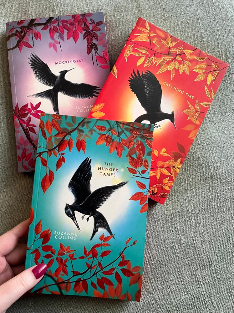 The Deluxe Editions of the Hunger Games Series by Suzanne Collins. Book covers of The Hunger Games, Catching Fire, and Mockingjay.  