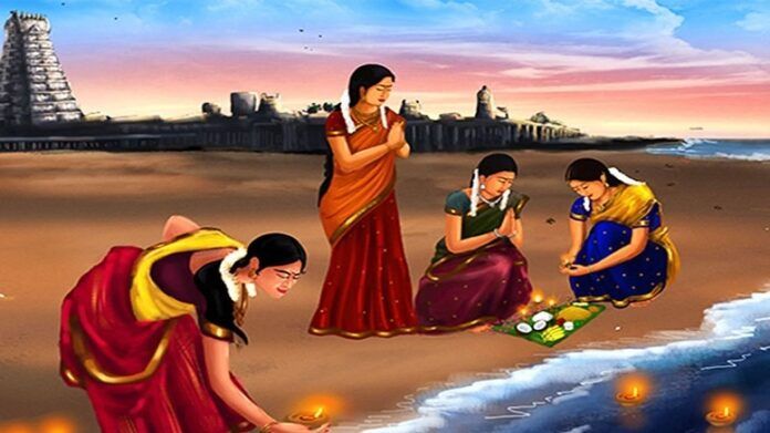 Women in saris doing pooja on the beach by the ocean with small lamps and temple in the background for festival of Aadi Perukku. 