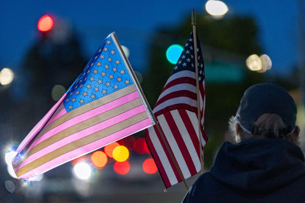 As much as I love to toot my own horn, I think this was actually my favorite shot of the evening. An unidentified supporter of democracy stands at the intersection as night is falling. He is facing away from the camera, a blue baseball cap over his graying hair. He carries 2 American flags, one of which is glowingly backlit by the out of focus traffic lights and car headlights. Thanks again, Gus.