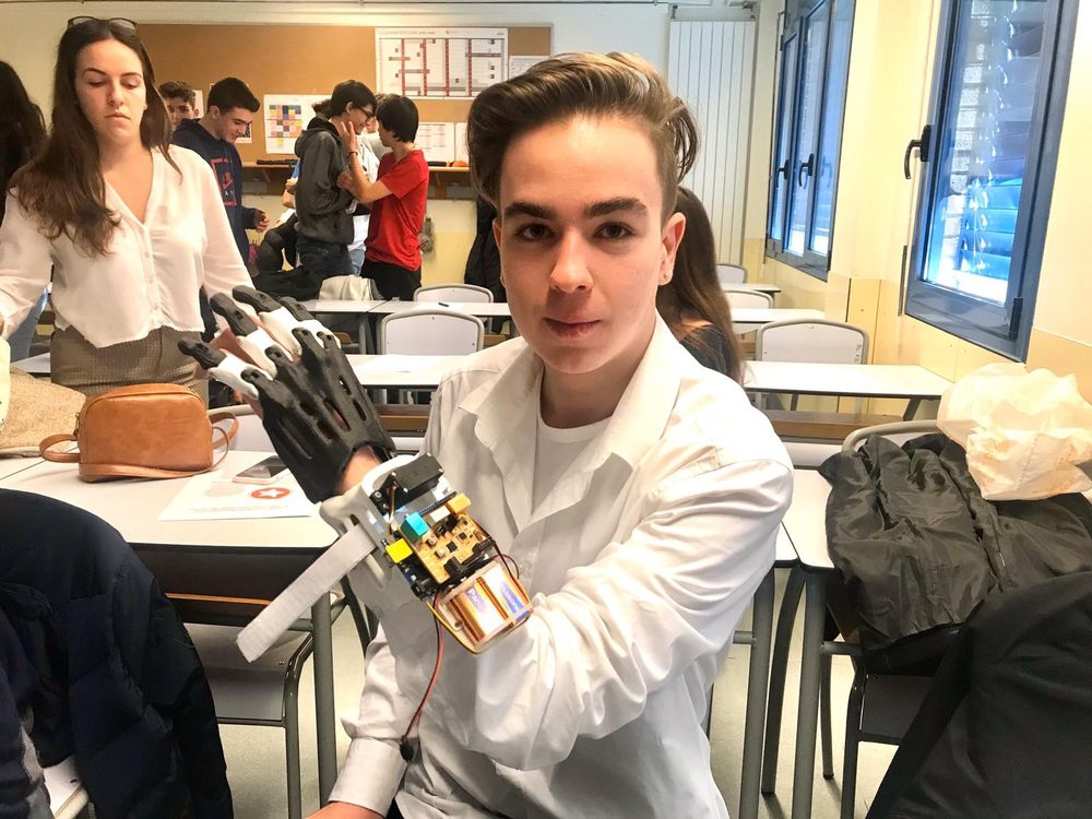 A teenager wearing white lab coat and a low-cost myoelectric hand prosthesis that he made himself using parts of Backyard Brains' Claw device.