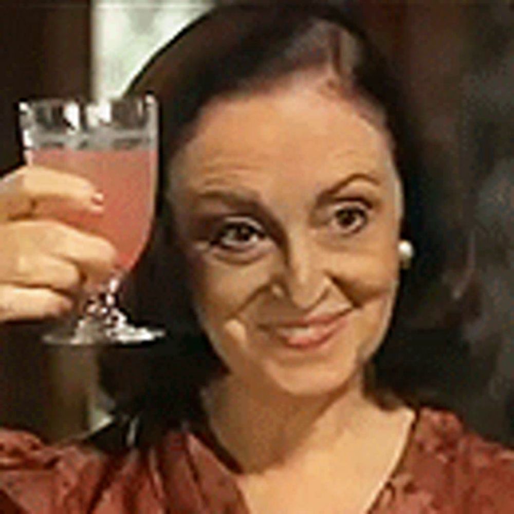 a woman is holding a glass of pink liquid in her hand and smiling .