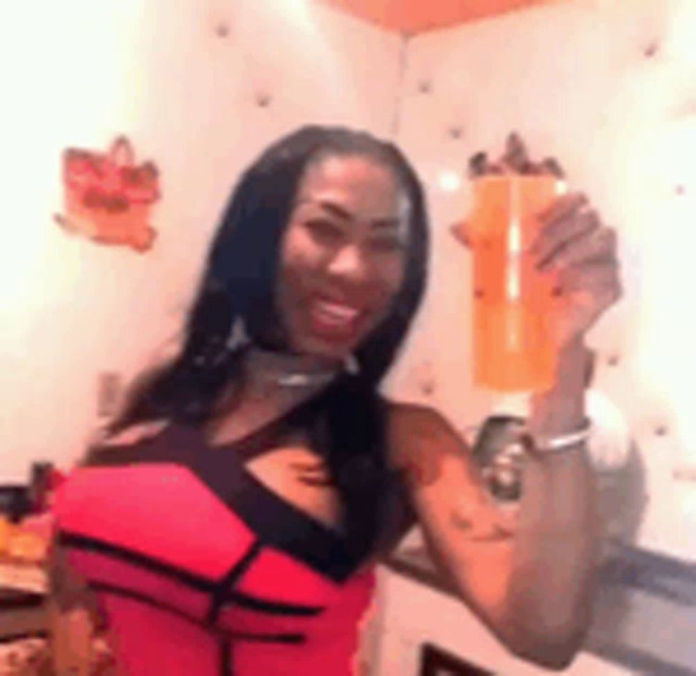 a woman in a pink tank top is holding a cup of orange juice .