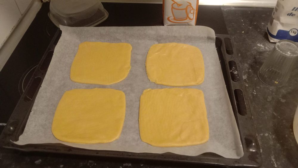 squares of thinly rolled dough with rounded angles. the plastic container used to cut these out is seen in the corner