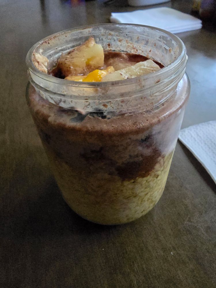 A side view of Cold oatmeal, which features mangos, pineapples, visible on the top, along with a layer of toppings then the oatmeal itself 