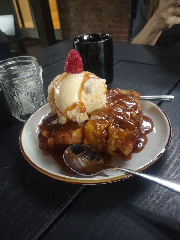 Bread pudding covered in caramel sauce with a scoop of vanilla ice cream on top.