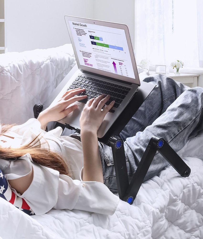 A person in bed working on a laptop which sits on an adjustable table 