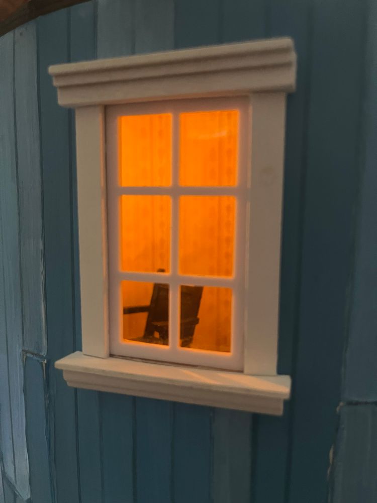 The spare room window lit up with yellow light. Through the window you can see a small office chair. 