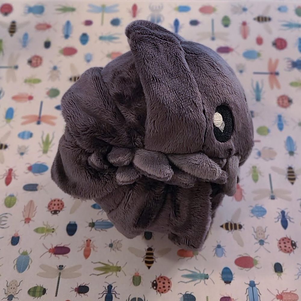Individually made plush grey isopod curled up side view 
