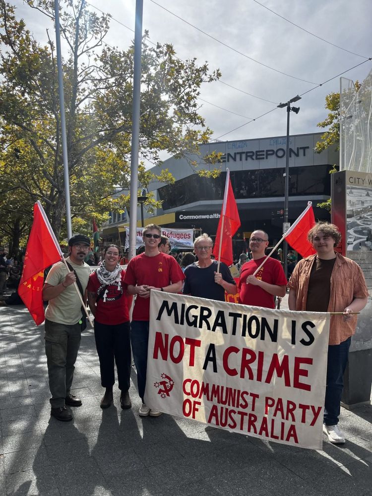 Group of people with red flags behind a banner reading 'Migration is not a crime: Communist Party of Australia