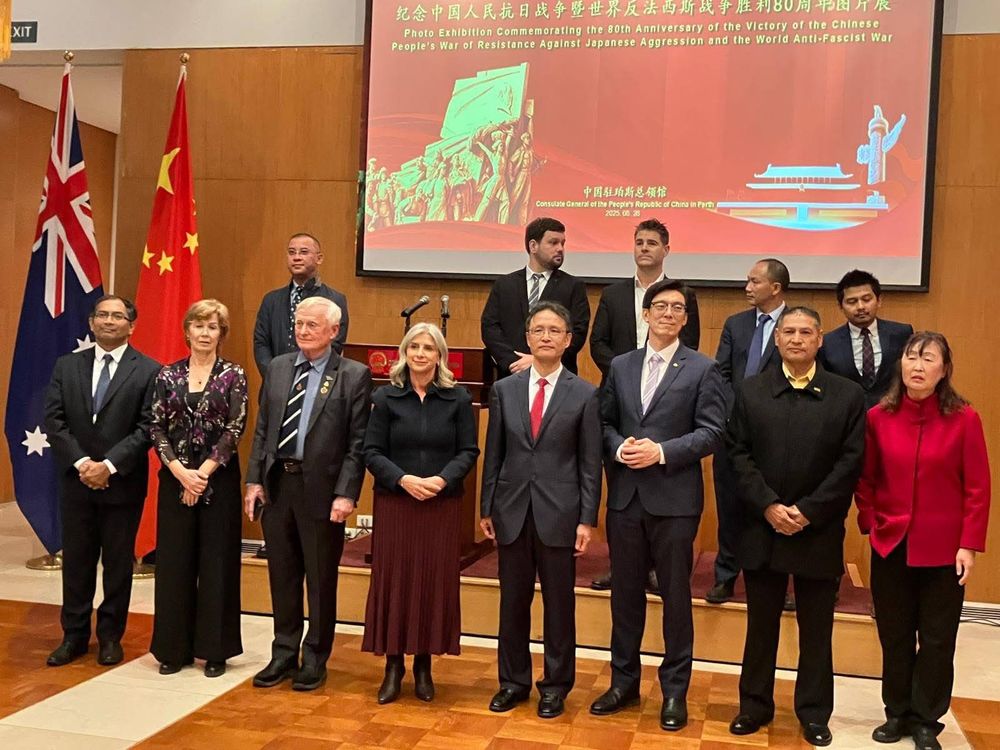 A group picture in front of a slide depicting heroic Chinese people and an explanation in Chinese and English that it's the anniversary of victory in the anti-fascist war