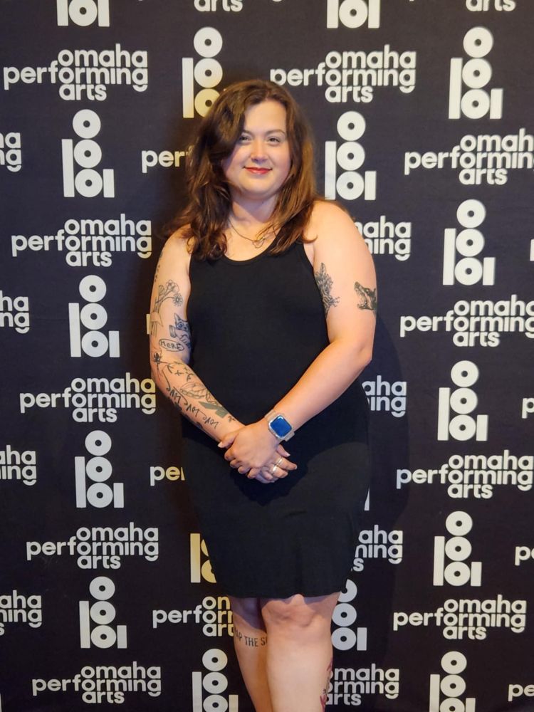 Rikki standing in front of the Omaha Performing Arts photo background wall.