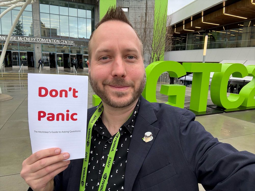 Photo of Eliot at GTC holding “the hitchhiker’s guide to asking questions”