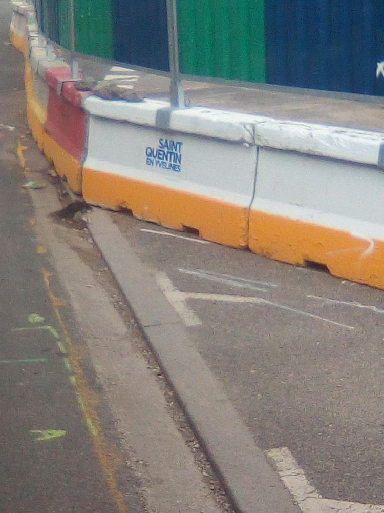 une barrière de béton qui entoure des travaux, et dessous, un tag au pochoir qui dit "Saint Quentin en Yvelines"