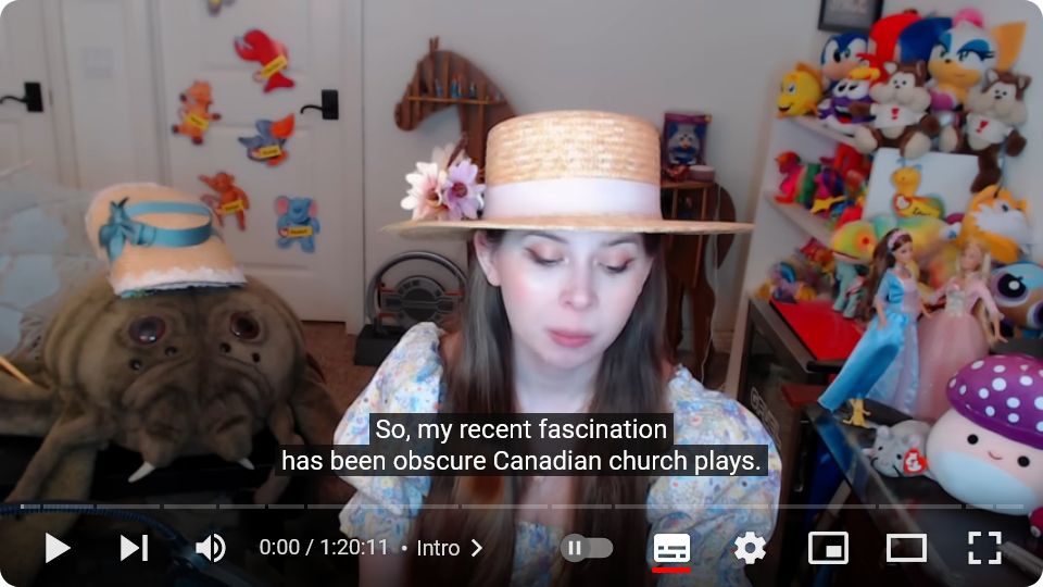Jenny Nicholson dit "donc ma fascination du moment, c'est les pièces canadiennes obscures d'églises". Elle est habillée en tons pastel et porte un chapeau de paille à fleur, dans le fond il y a plein de peluches dont une énorme peluche d'araignée qui a aussi un chapeau.