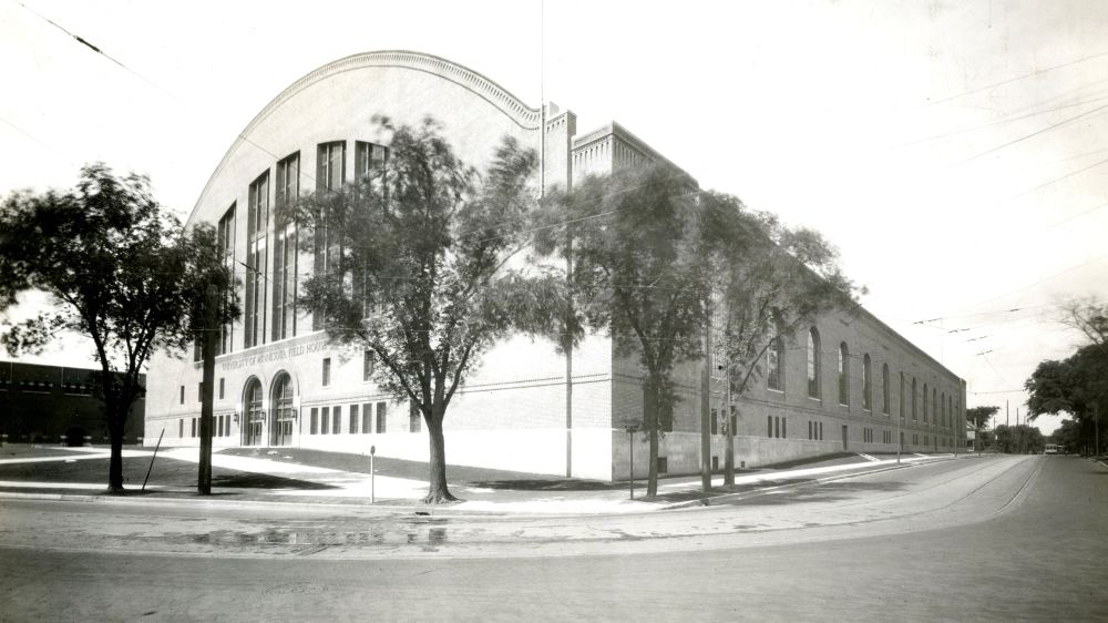 The completed "Field House" in 1930 at intersection of 4th Street SE and Oak Street SE. A large brick building takes up the block, arched roof is apparent on the East facade where the arched front doors are. Streetcar tracks in the foreground. 