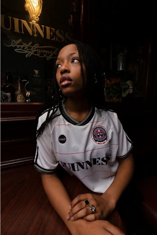 Frau im neuen Bohemians Dublin Trikot vor einem Guinness-Spiegel.