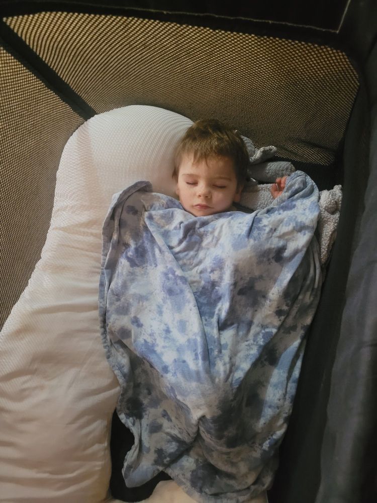 Small human child wrapped in a blanket. Sleeping in his play pen.