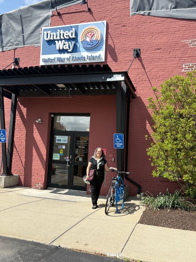 Rebecca wearing black standing with her bicycle at the front of the United Way building with sign above. 