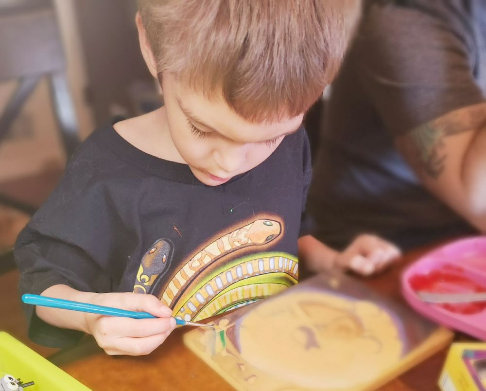 Artist's 5 year old son very focused on painting part of on a surprise art piece, blurred for secrecy.