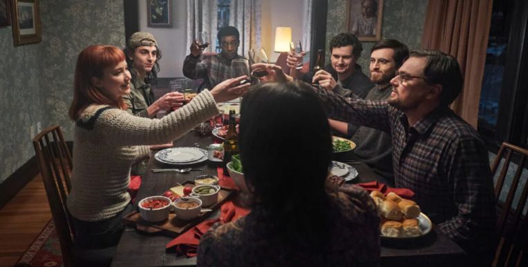 Group of people sitting around table touching glasses in a toast before a meal. The scene is from the end of the movie, "Don't Look Up."