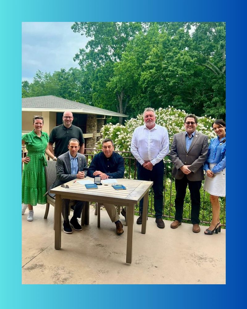 Childlight CEO Paul Stanfield and Child Rescue Coalition CEO Greg Schiller sign a memorandum of understanding on a table outside. Members of both teams stand behind them. 