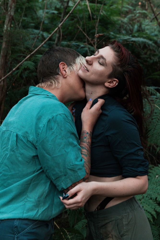 Two models embracing against a backdrop of ferns, wearing workwear 