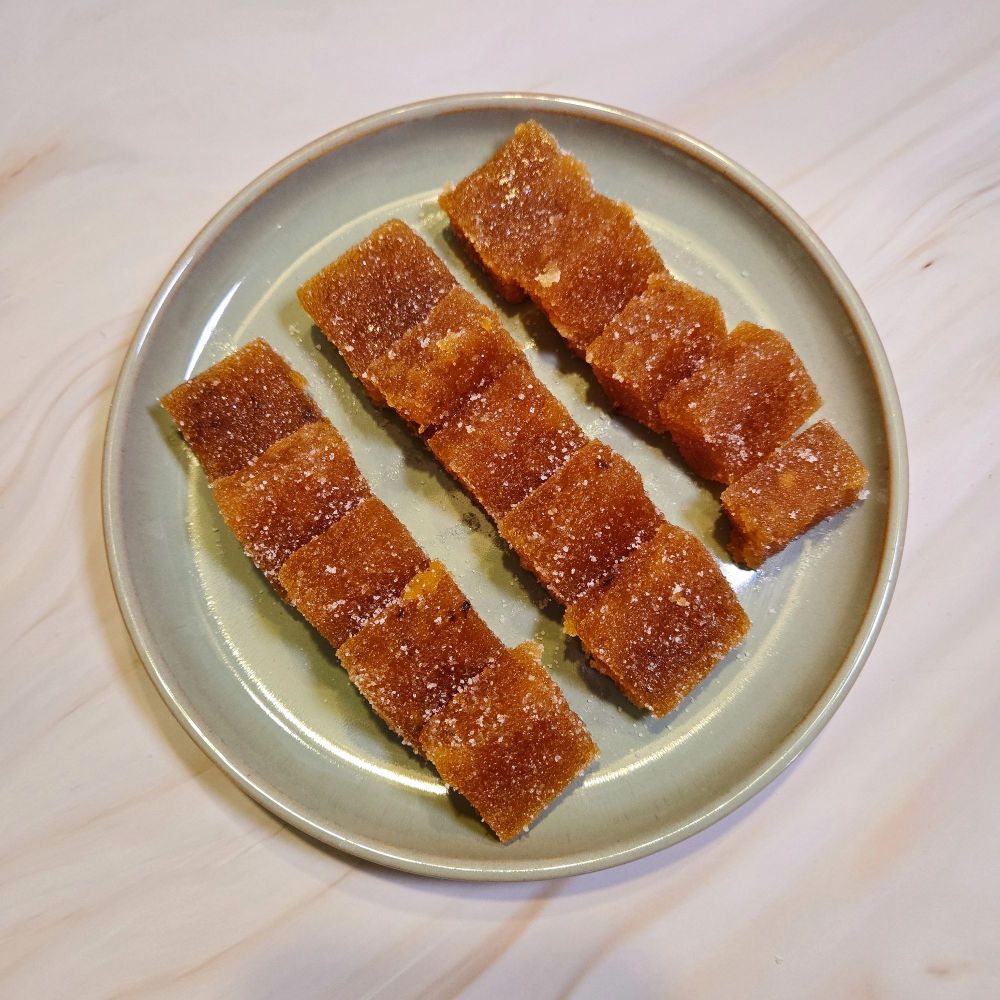 Green plate on a marble backdrop. The plate has square, orange/brown colored apricot fruit squares coated in sugar. 
