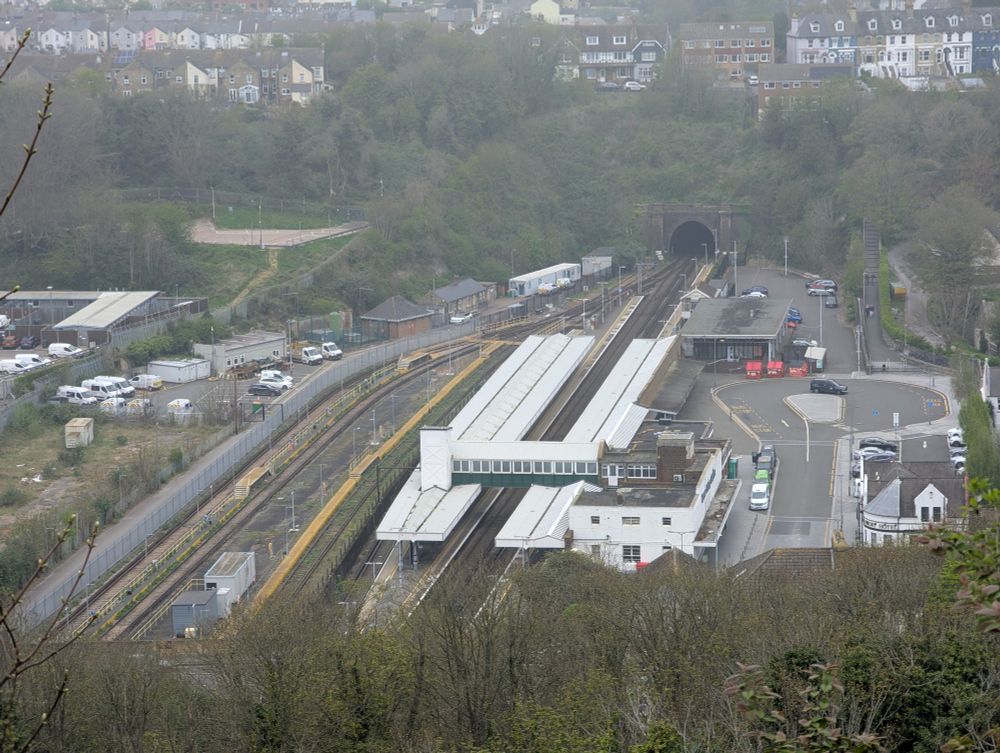 Dover Priory station seen from a nearby hill. Sidings to the left, a three platform station in the centre with canopies and station building 
At the top a tunnel mouth can be seen