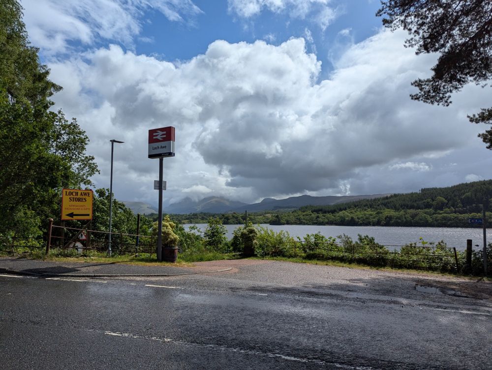 Double arrow sign for Loch Awe on the side of a road. The loch in the background with mountains in the far distance 