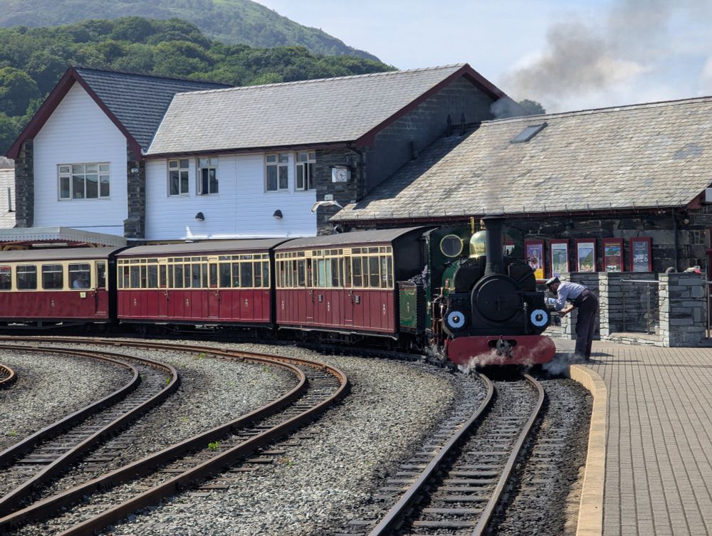 Ffestiniog loco in the platform with the station building behind, looking comparatively smaller than the WHR ones