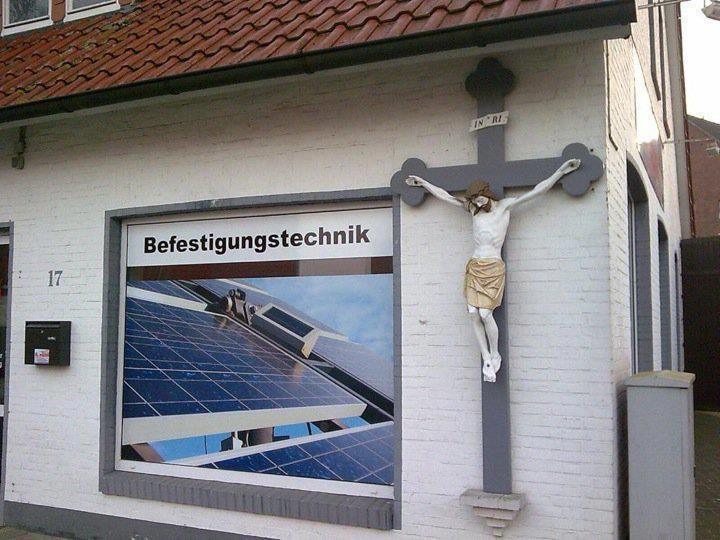 Das Bild zeigt die Außenansicht eines Gebäudes mit einer großen Werbung für die Installation von Solarmodulen und einem Kruzifix.

Gebäudeäußeres: Das Gebäude hat eine weiße Fassade und ist mit roten Dachziegeln geschmückt. Es gibt eine Adresstafel mit der Nummer “17”.
Werbungstafel: Eine große Tafel zeigt ein Bild von Solarmodulen, die auf einem Dach installiert werden. Das Wort „Befestigungstechnik“ ist deutlich zu sehen, was auf den technischen Aspekt der Installation von Solarmodulen hinweist.
Kruzifix: An der Wand neben der Werbetafel ist ein Kruzifix angebracht. Das Kruzifix besteht aus einem grauen Kreuz und einer weißen Statue von Jesus Christus mit ausgebreiteten Armen und drapierter Kleidung.
Die Kombination aus moderner Solartechnologie und dem traditionellen Symbol des Kruzifixes erzeugt einen bemerkenswerten visuellen Kontrast.