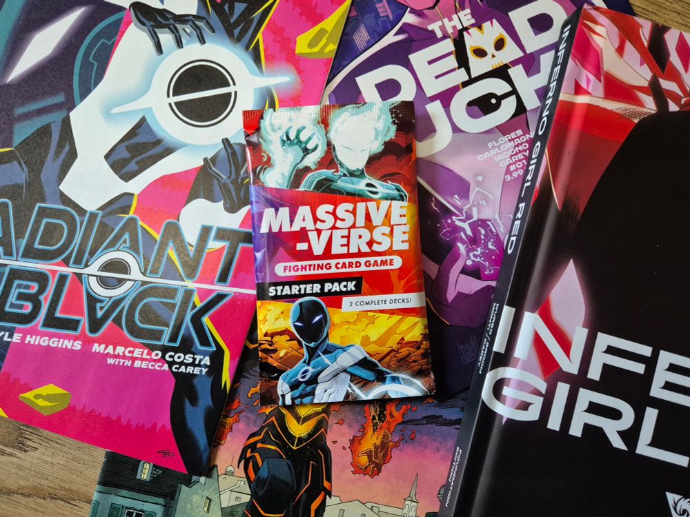 The new Massive-Verse Fighting Card Game starter pack sitting stop various comics from the Massive-Verse range, including Radiant Black, The Dead Lucky, Rogue Sun, and the Inferno Girl Red graphic novel. 