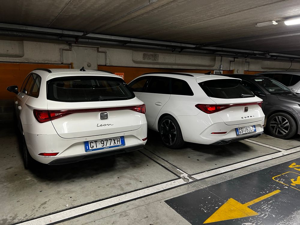 A white Seat Leon Estate parked next to a white Cupra Leon in an Italian parking garage.