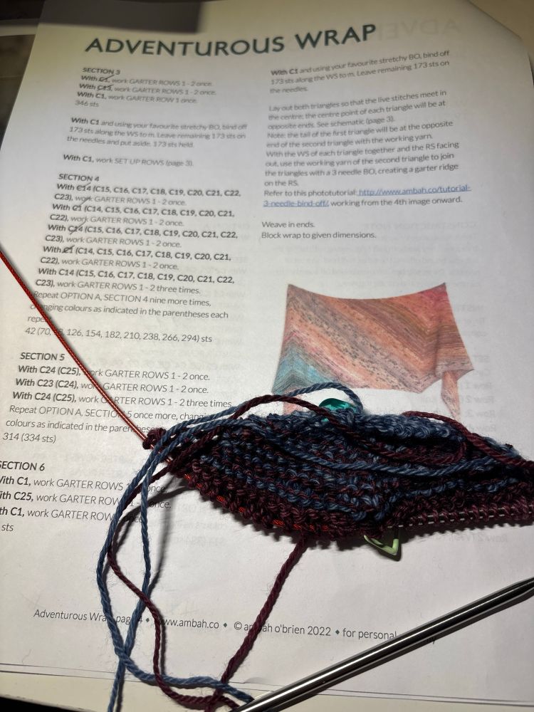Photo of some knitting on top of a knitting pattern for Adventurous Wrap