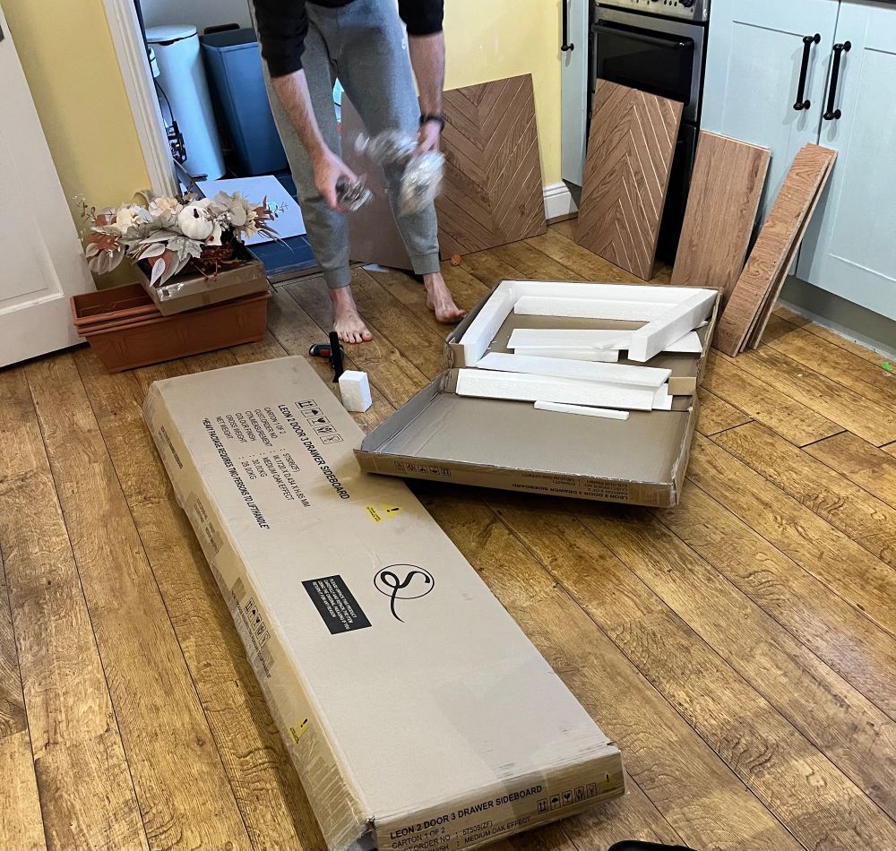 The legs and torso of eldest as he opens two large cardboard boxes which contain a side board all flat packed! 