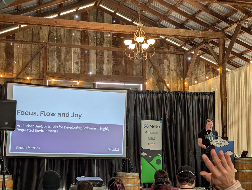 A photo of Simon on stage as attendees raise their hands in agreement about lunch being delicious.