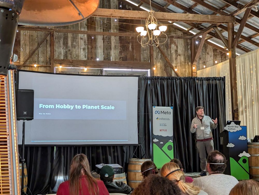 A photo of Mike on stage beginning his talk with his title slide on screen.