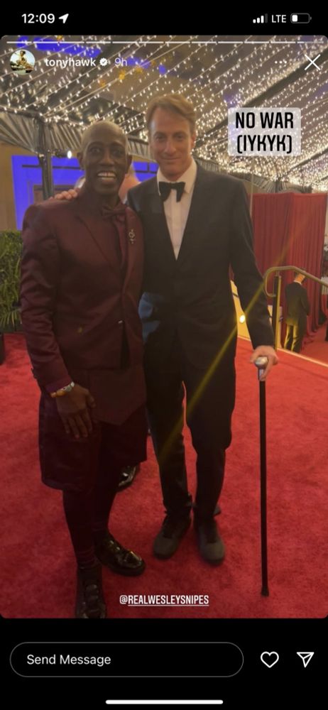 Foto publicada nos stories do Instagram de Tony Hawk. Ele aparece de smoking preto e gravata borboleta, apoiado em uma bengala, ao lado de Wesley Snipes, que veste um terno vinho com bermuda no mesmo tecido, meias combinando e sapatos pretos brilhantes. Os dois estão sorrindo em um tapete vermelho, com um teto cheio de luzes decorativas ao fundo.

No canto superior direito da imagem, está escrito: “NO WAR (IYKYK)”.
Na parte inferior, a marcação: @REALWESLEYSNIPES.