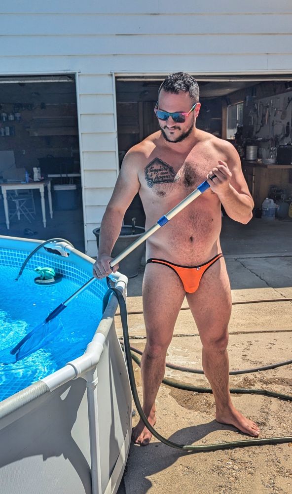 Rocky skimming an outdoor pool, wearing tiny orange briefs 