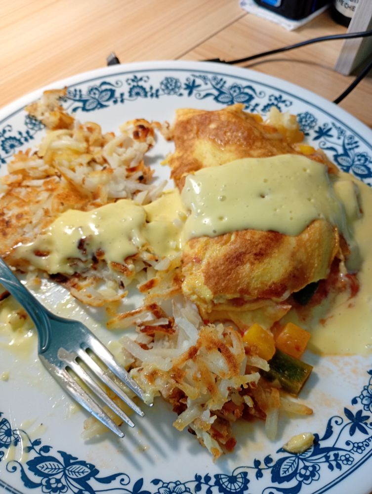 a corelle dinner plate with hash browns and an omelete on it
