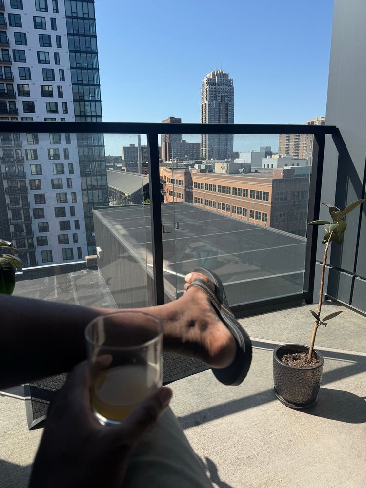 Man person sitting on balcony holding a drink looking at skyline. 