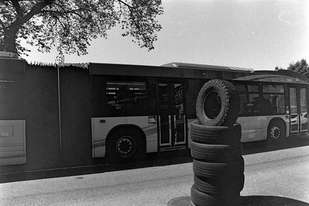 A stack of tires
The top one is standing on end
It’s in the road
A bus drives by 